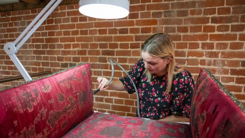 Conservator carefully vacuuming red sleeping chair from Ham House